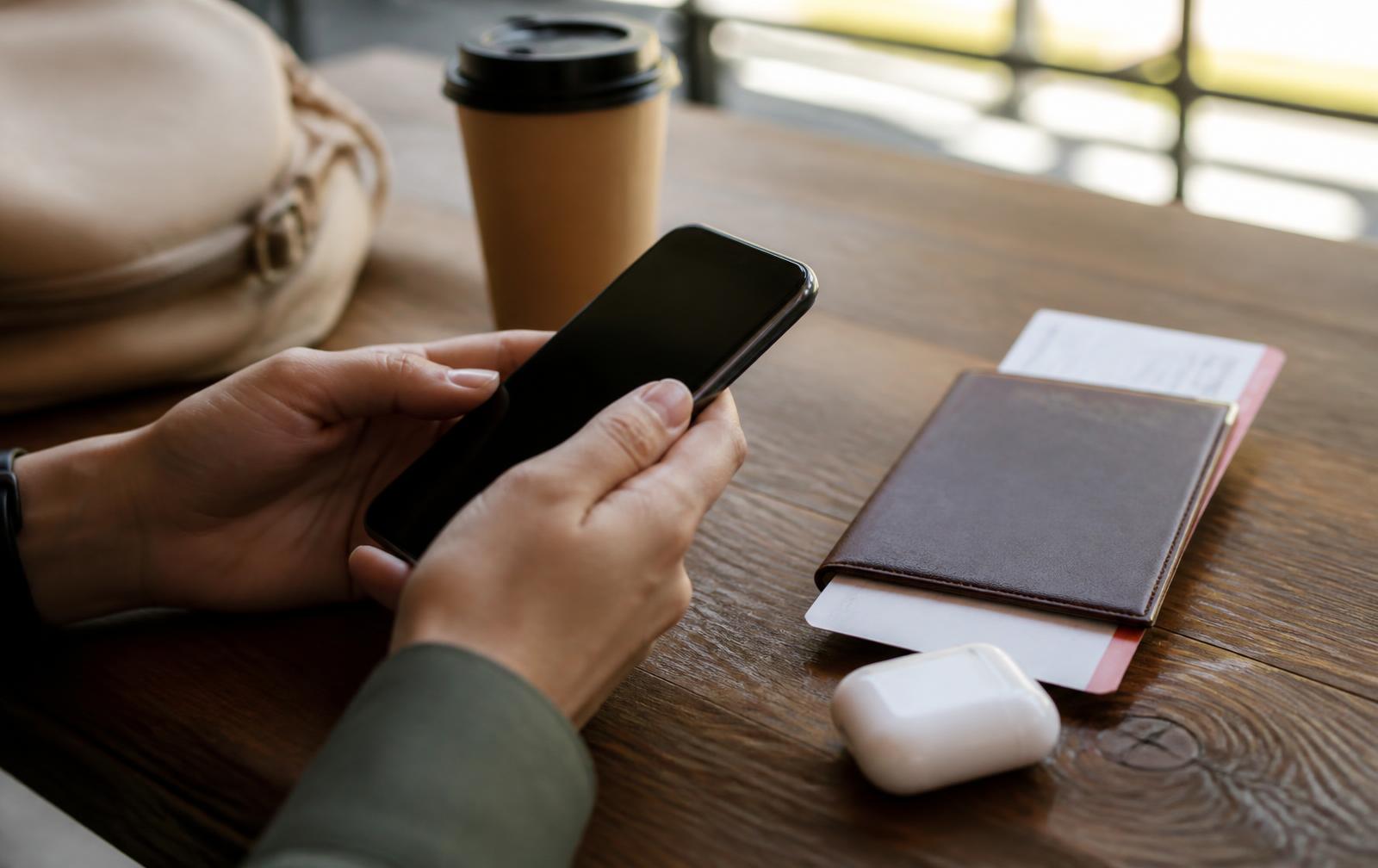 Phone, earbuds case, passport and boarding pass on a cafe table